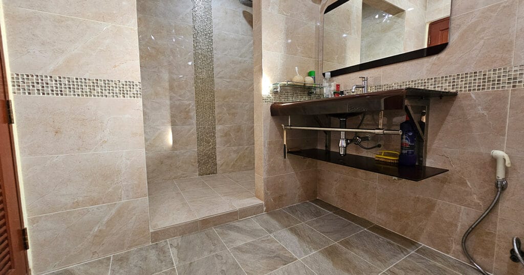 Modern Phuket villa bathroom with walk-in shower, mosaic tile feature, vanity sink, and tiled flooring.